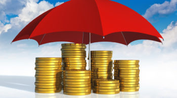 Financial stability, business success and insurance concept: stacked golden coins covered by red umbrella against blue sky with clouds on white background with reflection effect